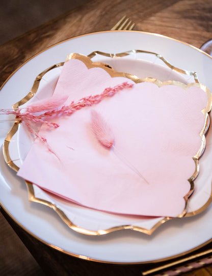 Mise en situation sur assiette des serviettes en papier à bords festonnés pour fête rose poudré et doré