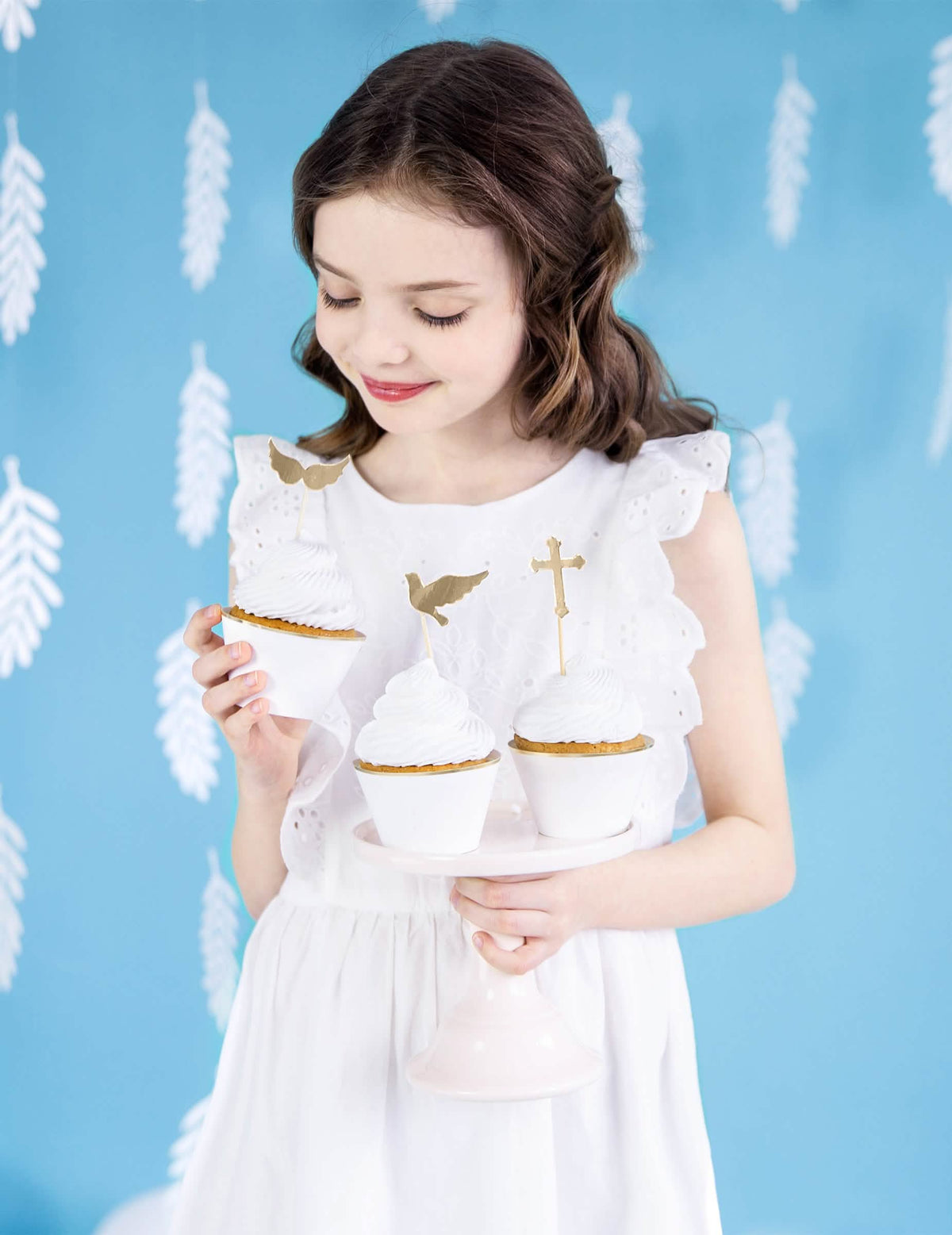 Mise en situation d'une enfant tenant les habillages à cupcakes en papier pour mariage blancs et dorés
