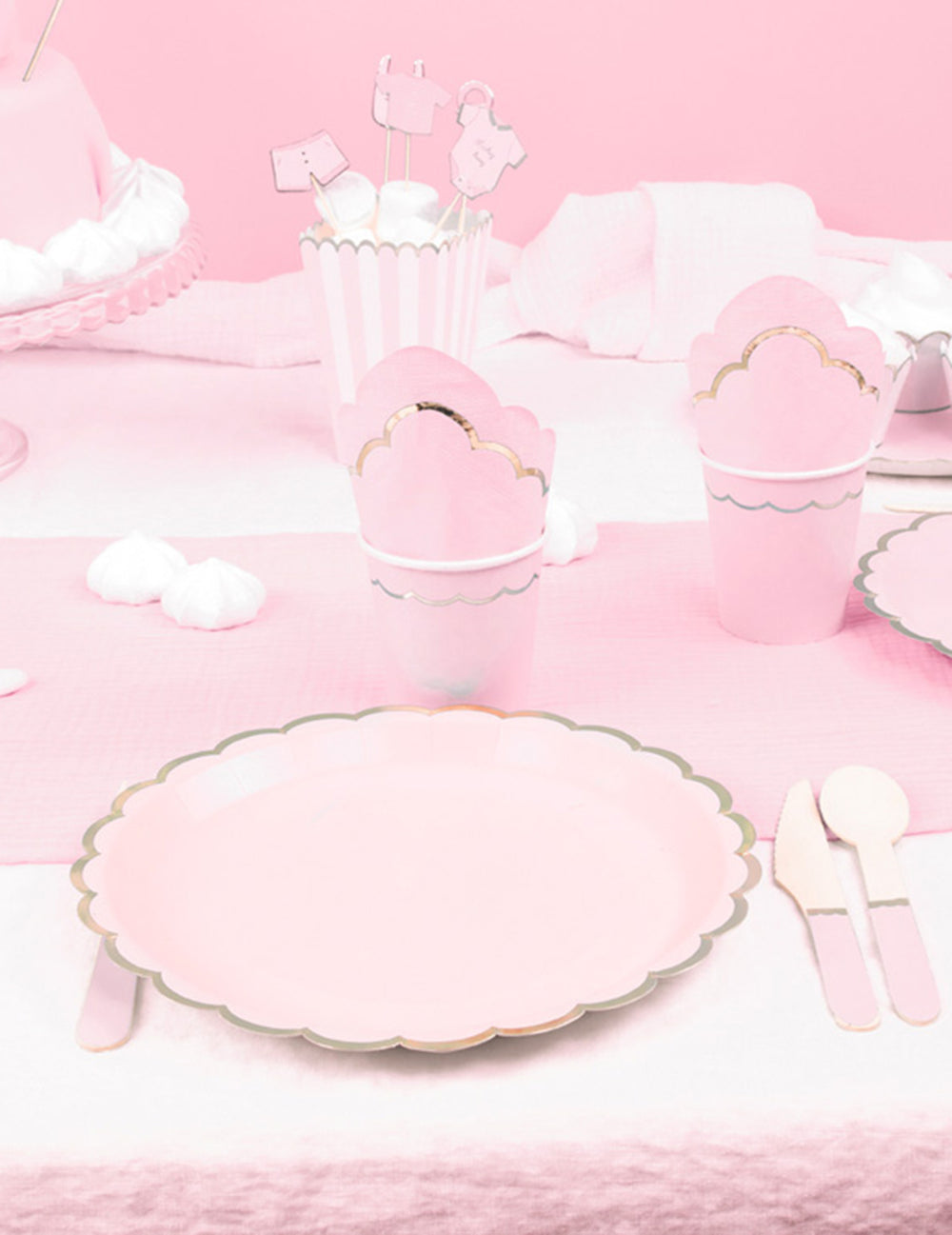 Mise en situation sur une table de fête des assiettes en carton festonnées rose pastel et or