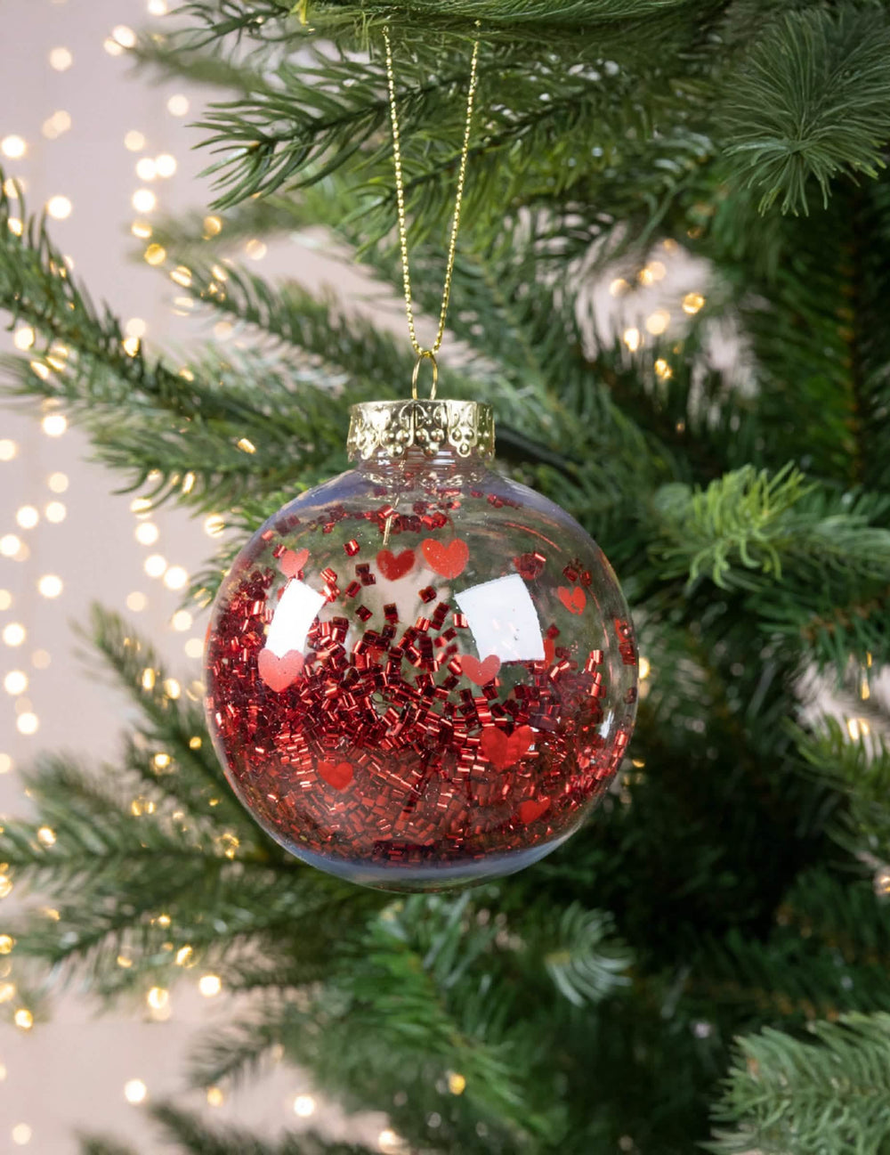 Hängende Ansicht in einem Weihnachtsbaum der Weihnachtskugel mit roten Herzen und glänzendem Konfetti