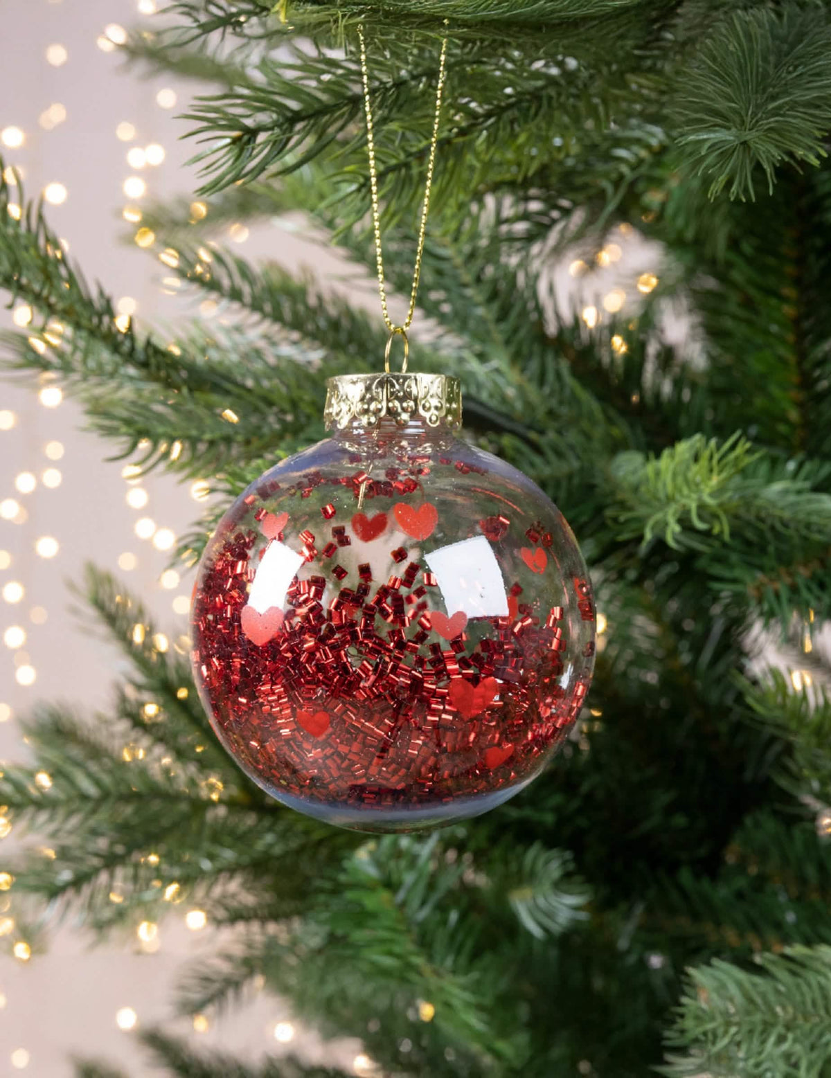Hängende Ansicht in einem Weihnachtsbaum der Weihnachtskugel mit roten Herzen und glänzendem Konfetti