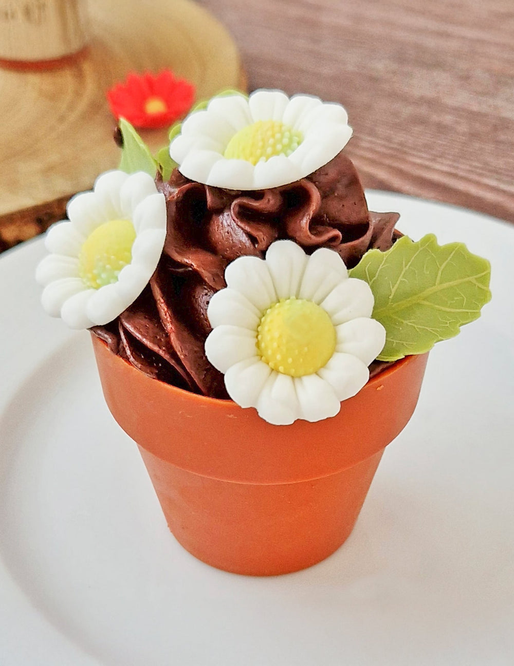 Mise en situation sur un dessert en pot de fleur des décorations en sucre marguerites et feuilles blanches et vertes