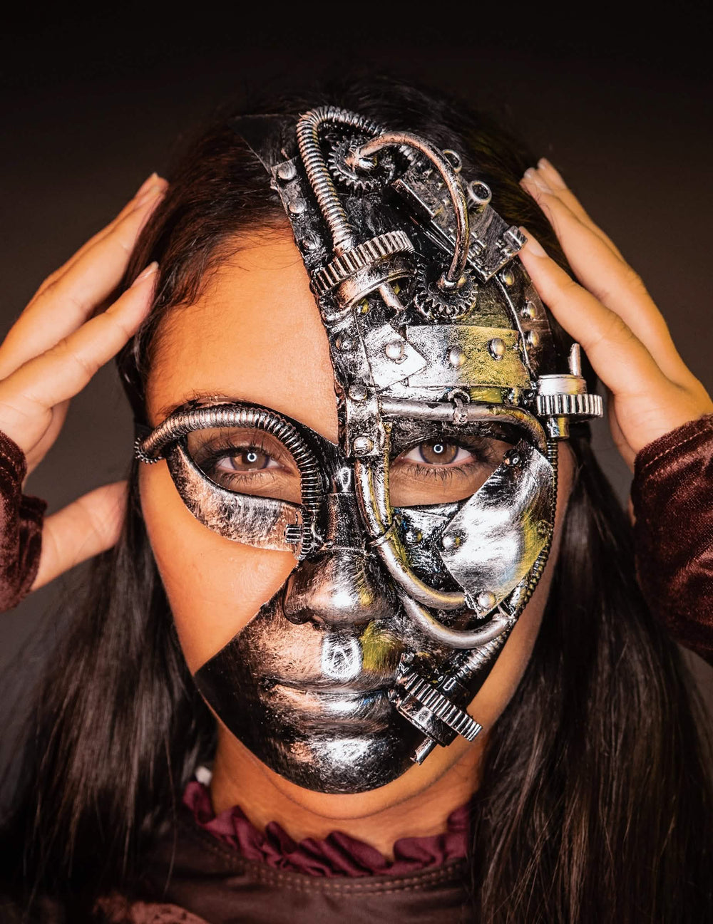 Frontansicht mit den Händen an den Schläfen der halben Steampunk-Roboter-Maske