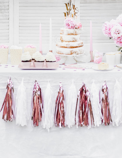 Mise en situation sur une table de la guirlande tassel 12 pompons pour décoration de fête rose gold métallisé